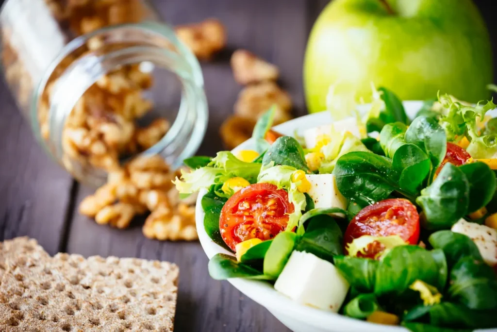 Fresh anti-aging salad with greens, cherry tomatoes, avocado, and cheese, served with green apple, walnuts, and whole grain crackers.