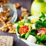 Fresh anti-aging salad with greens, cherry tomatoes, avocado, and cheese, served with green apple, walnuts, and whole grain crackers.