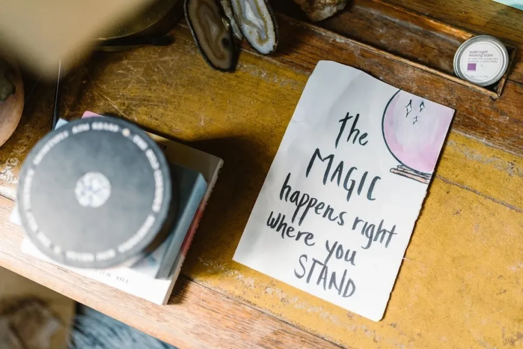 Inspirational affirmation on a wooden desk reading "The magic happens right where you stand".