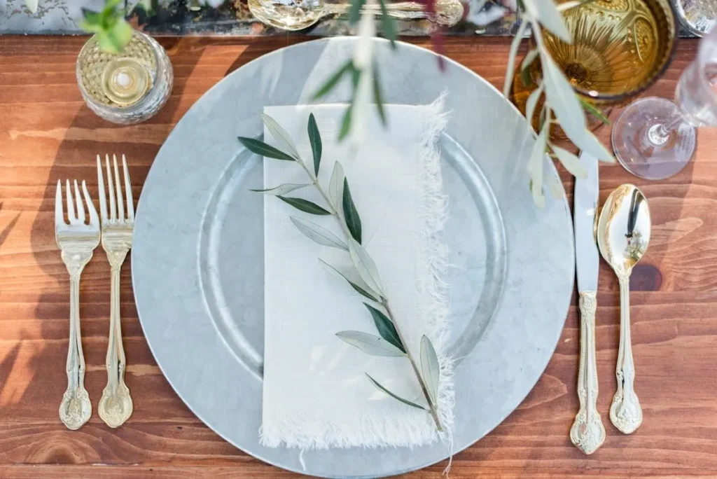Elegant white plate with silver cutlery and olive branch on a wooden table.