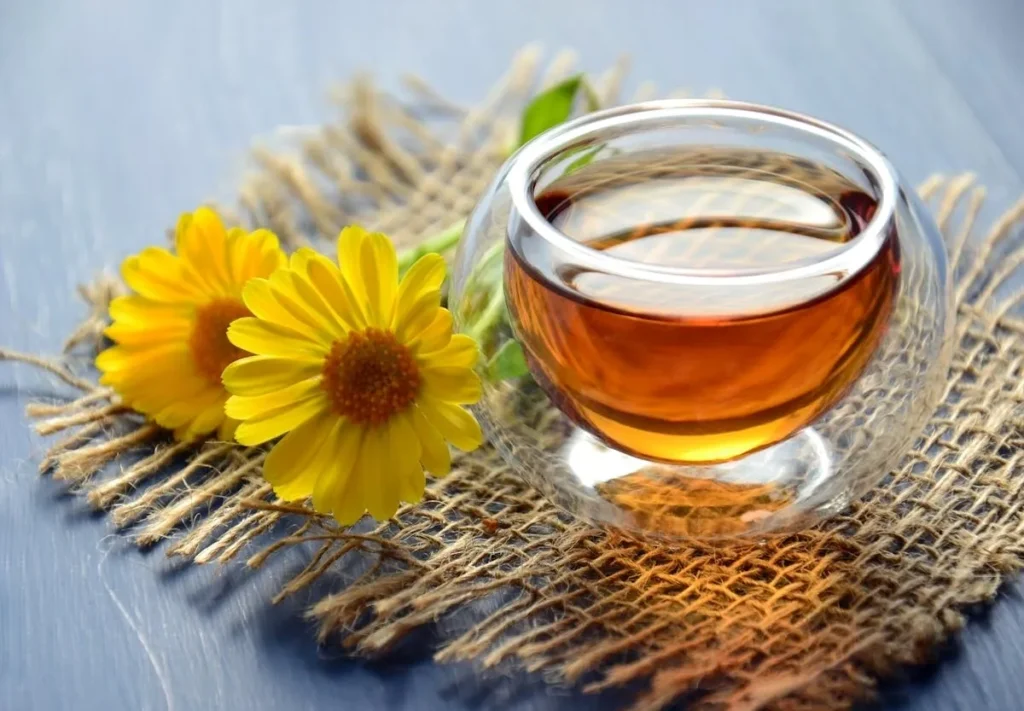 Chamomile tea in a glass cup with yellow flowers on wooden table.