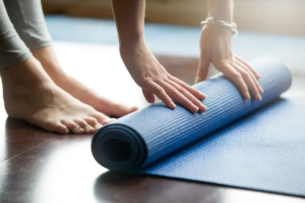 Woman rolling blue yoga mat on wooden floor before yoga practice.